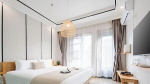 Een moderne hotelkamer met een groot bed, nachtkastje, televisie en raam met gordijnen.