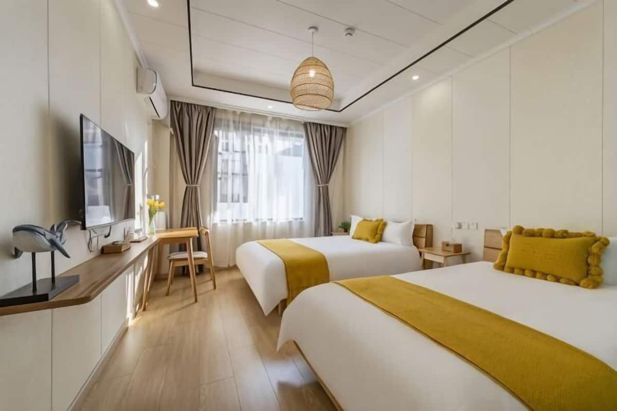 Habitación de hotel con dos camas, un escritorio, una silla, un televisor y una ventana con cortinas.