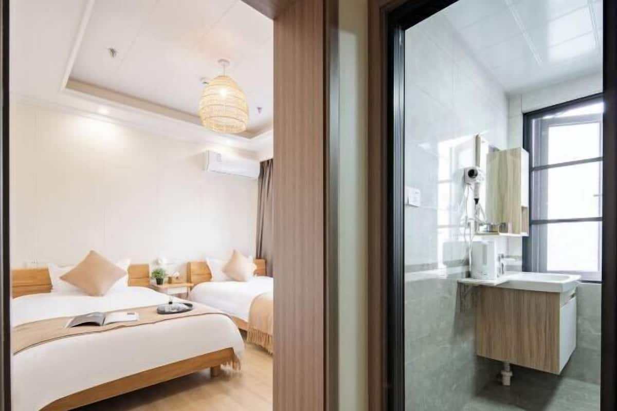 Habitación de hotel con dos camas, un ventanal grande, un baño moderno con lavamanos y espejo, y una lámpara colgante.