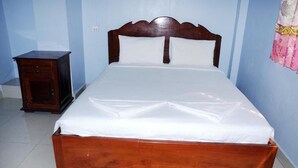 Een enkel bed met houten frame en witte beddengoed in een kamer met lichtblauwe wanden en een betegelde vloer.