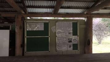 Un espace extérieur abrité, doté d’un banc en bois, d’un panneau d’affichage où sont accrochés des documents et d’un toit en métal.