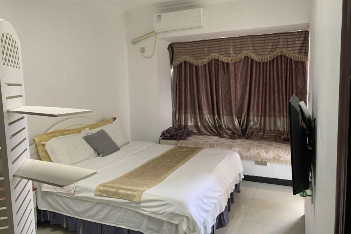 Una cama individual con cabecera, una mesita de noche, un televisor y una ventana con cortinas.