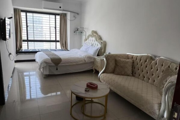 A hotel room with a bed, a sofa, a small table, and a window with curtains.