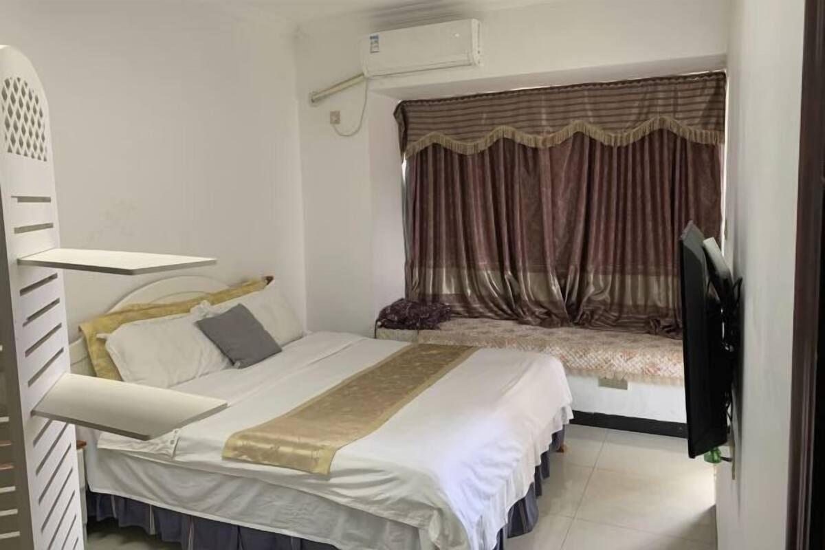 A bedroom with a bed, a TV, and a window with curtains.