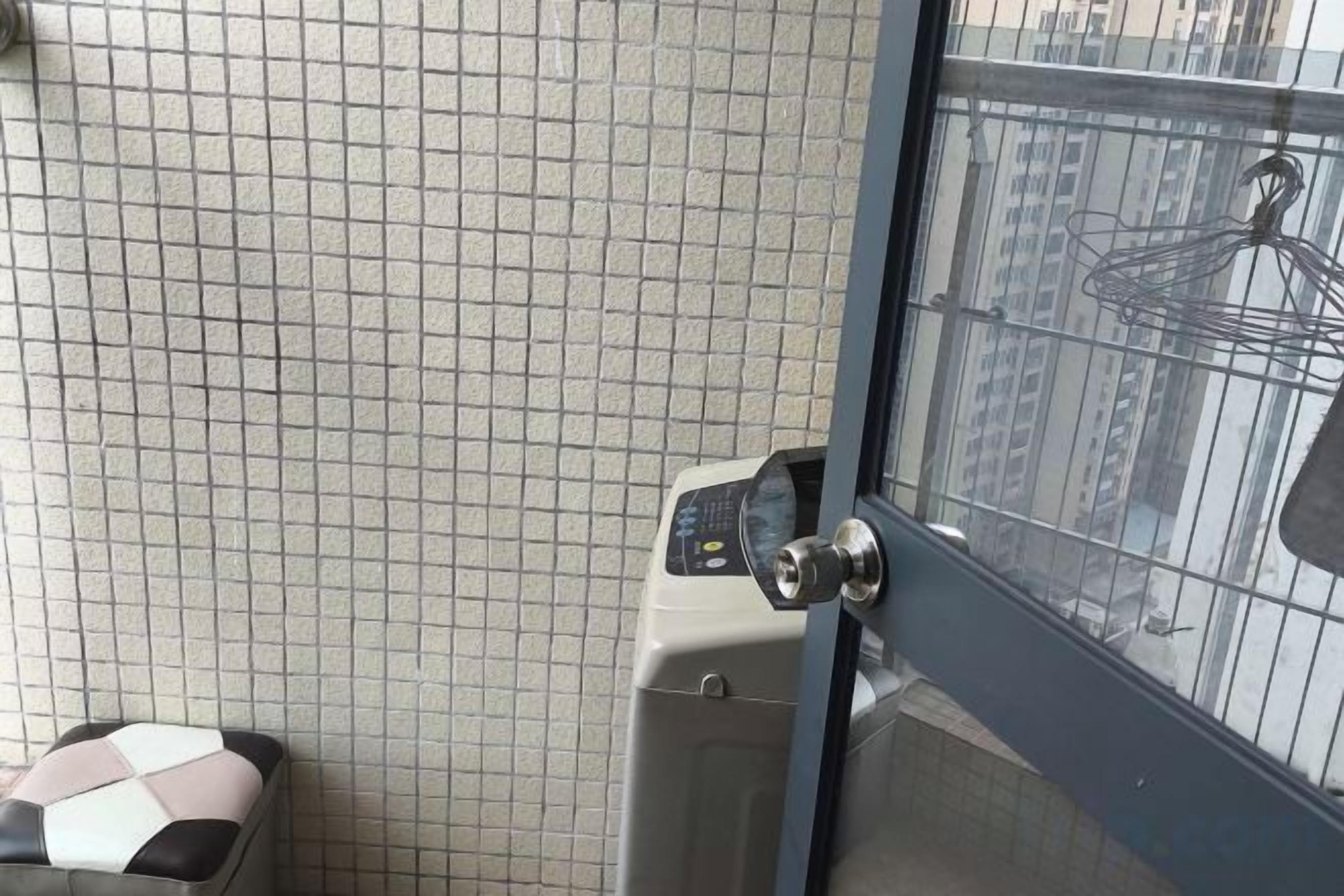 A room with a tiled wall, a washing machine, and a door with a view of buildings.