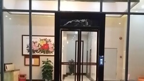 Entrada de hotel con puerta de vidrio, un mostrador de recepción y una planta en maceta.