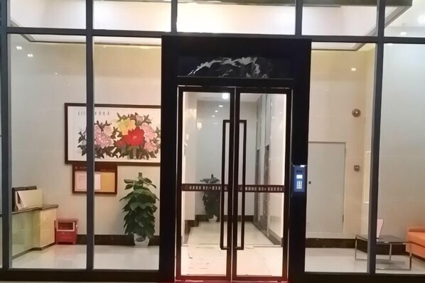 A hotel entrance with a glass door, a reception desk, and a potted plant. - Enping Jinjiang International New Town Apartment (Enping)