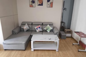 A modern living room with a grey sectional sofa, a white coffee table, and a small desk with a chair. - Enping Jinjiang International New Town Apartment (Enping)