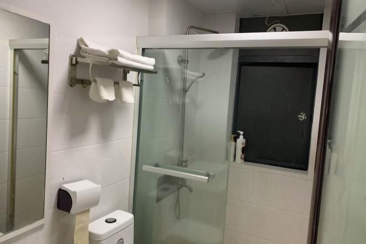 Un baño moderno con ducha envuelta en vidrio, un inodoro con dispensador de toallas de papel y un perchero para toallas.