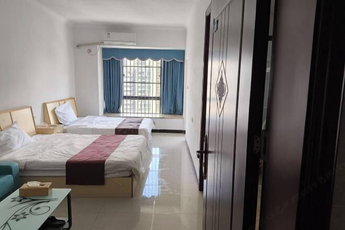 A hotel room with two beds, a desk, a chair, a window with curtains, and a wardrobe.