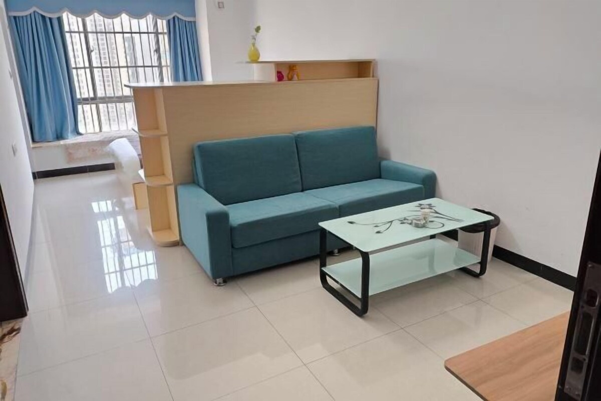 Una sala de estar con un sofá azul verdoso, una mesa de centro de vidrio y una estantería de madera.