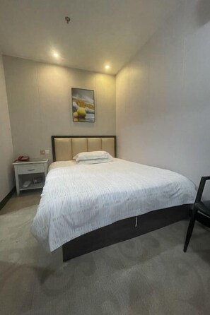 A hotel room with a bed, a nightstand, a chair, and a painting on the wall. - Xidu Hotel (Jiashan)