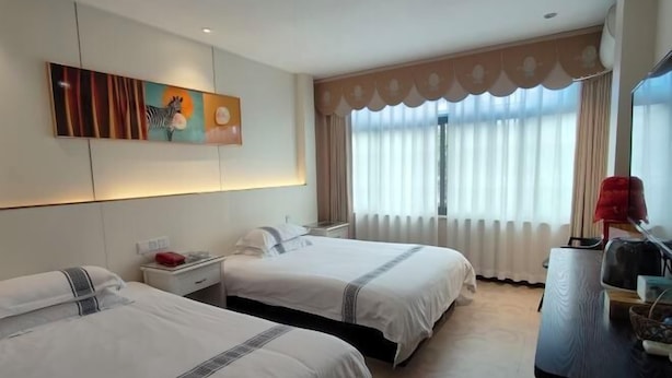 A hotel room with two beds, a painting on the wall, a window with curtains, and a desk with a lamp. - Xidu Hotel (Jiashan)