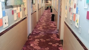 A hotel hallway with a floral carpet, wall-mounted light switches, and a trash bin. - Xidu Hotel (Jiashan)