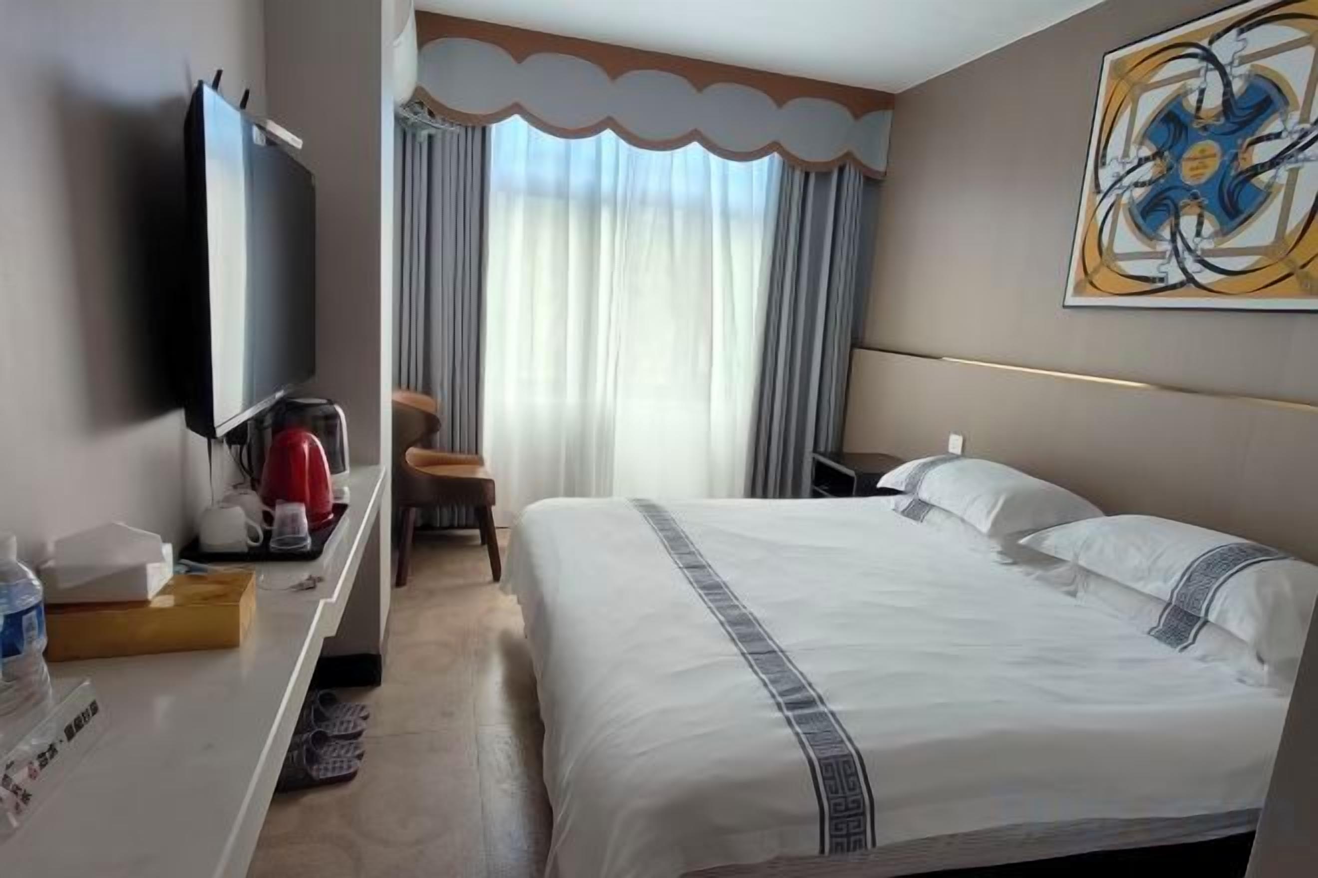 A hotel room with a bed, a desk with a television, a chair, and a window with curtains.