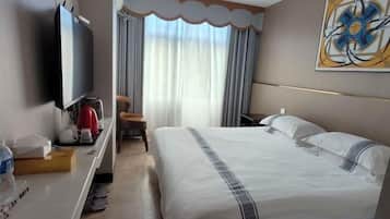 A hotel room with a bed, a desk with a television, a chair, and a window with curtains.