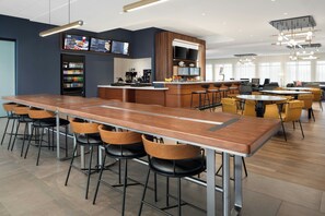 A modern bar area with long wooden tables, black and yellow chairs, a beverage dispenser, and a digital menu board. - Courtyard by Marriott Kodak Sevierville (Kodak)