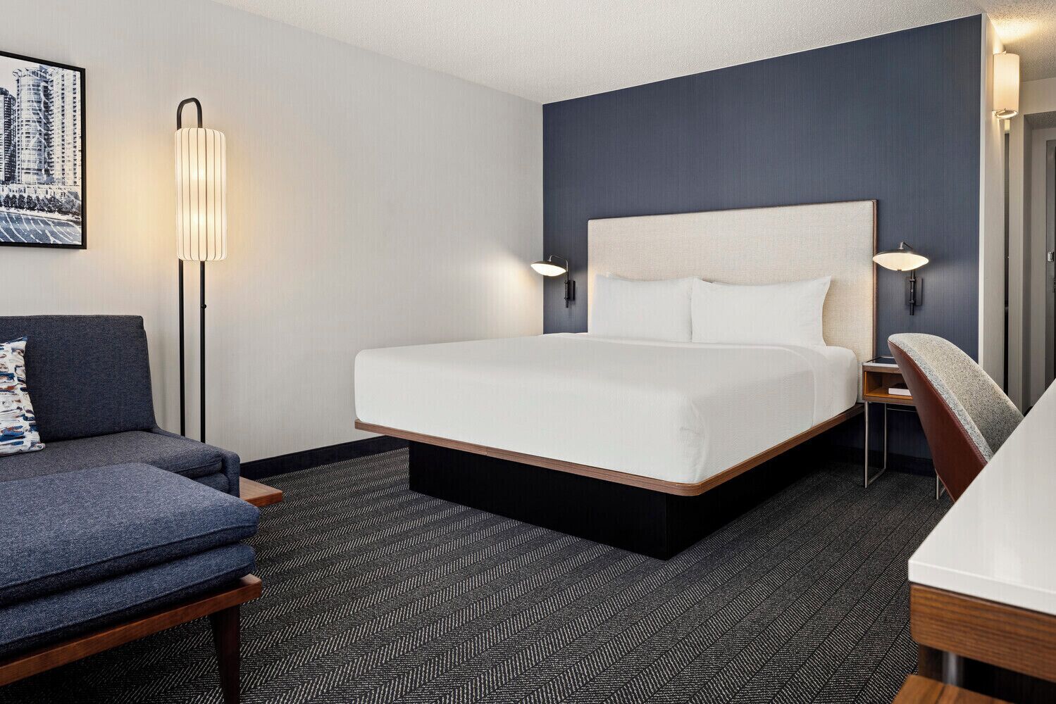 A hotel room with a large bed, a sofa, a desk, and a chair.