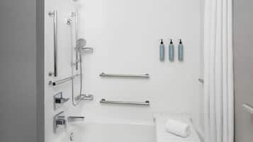 A modern bathroom with a bathtub, shower, and toilet. There are two towel bars, a hand dryer, and three bottles of hand soap on the wall.