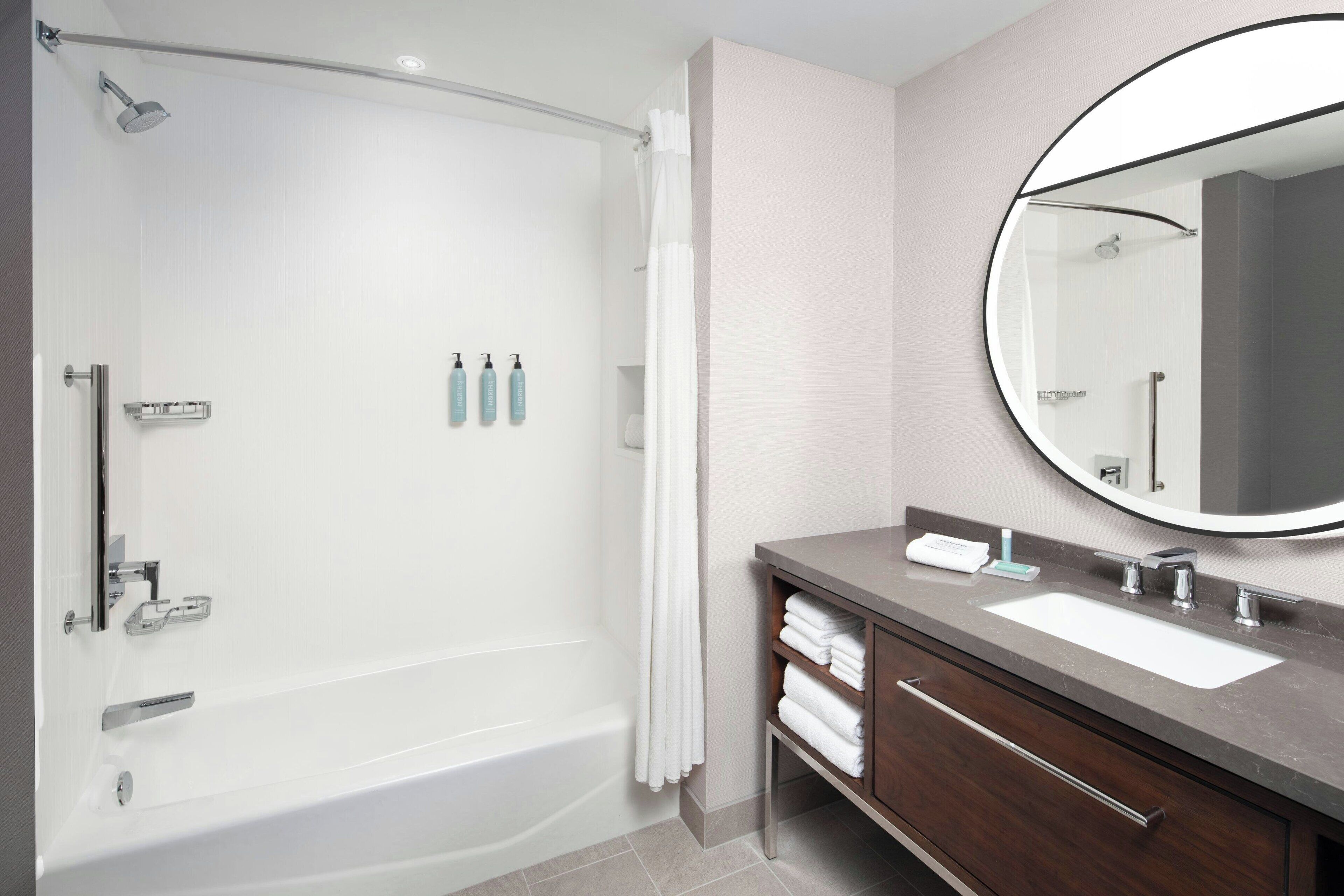 Une salle de bain moderne équipée d’une baignoire, d’un meuble-lavabo avec un évier, d’un miroir et d’articles de toilette.