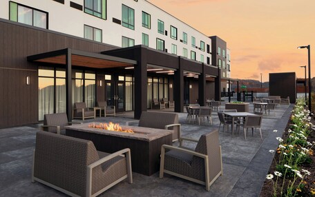 An outdoor patio with seating, a fire pit, and a view of a modern building.