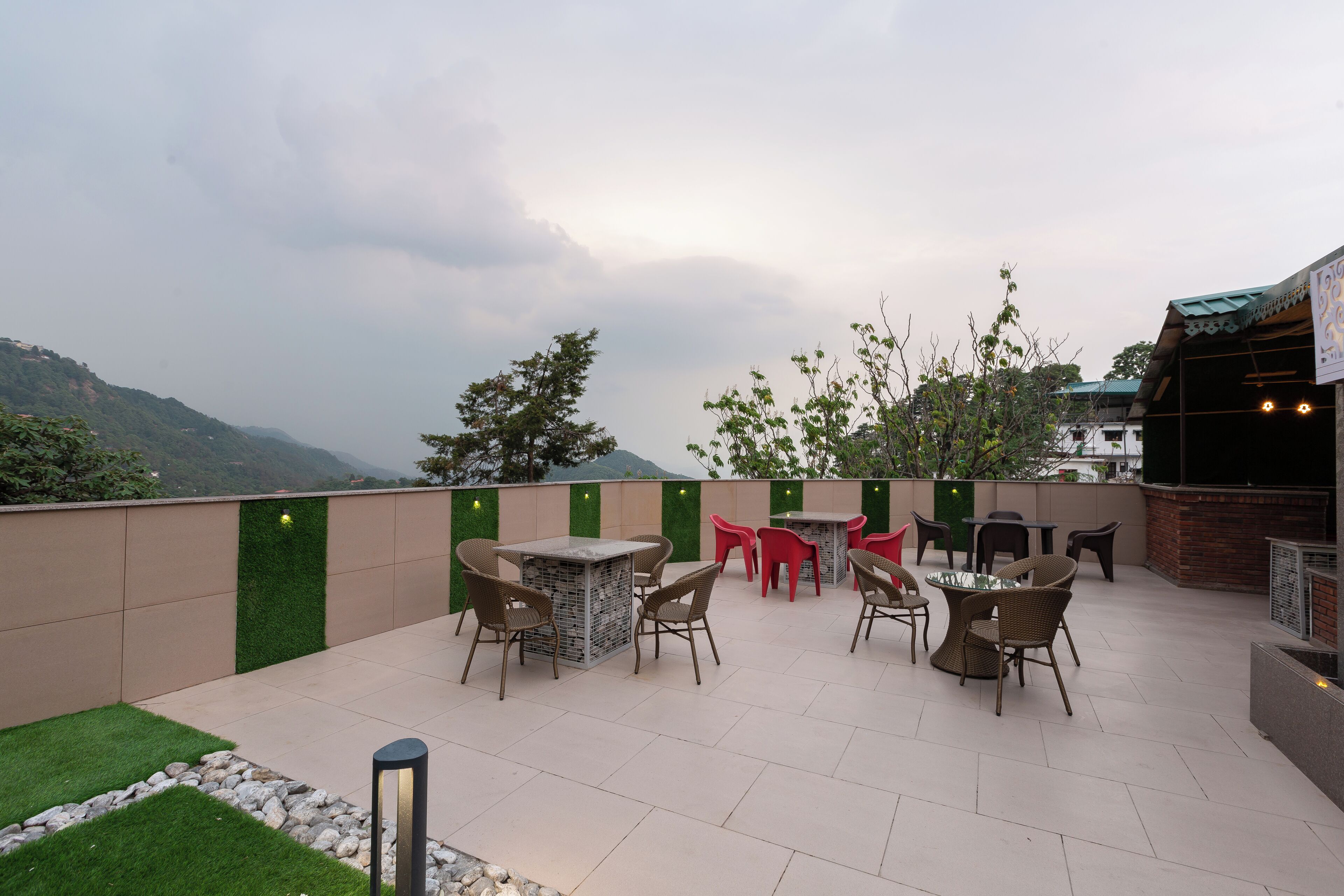 Een terras buiten met tafels en stoelen, een bakstenen muur en uitzicht op bergen.