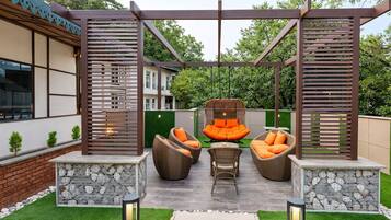 An outdoor seating area with wicker furniture and a hanging chair, surrounded by a wooden pergola structure.