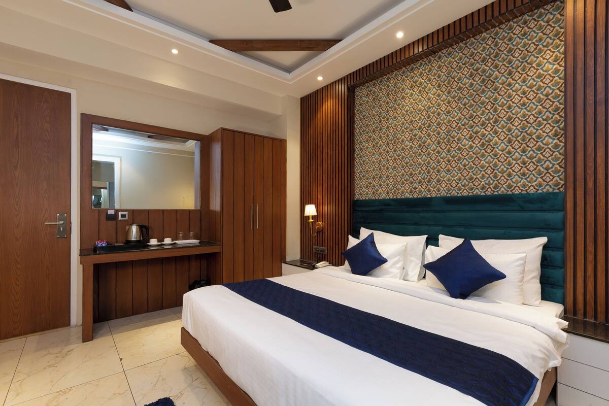 A hotel room with a bed, a desk, a mirror, and a patterned headboard.