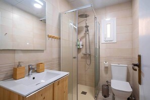Une salle de bain moderne avec une douche à parois de verre, un lavabo blanc doté de distributeurs de savon en bois et des toilettes.