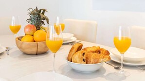 En frukostuppdukning med croissanter, frukt och apelsinjuice på ett vitt bord.