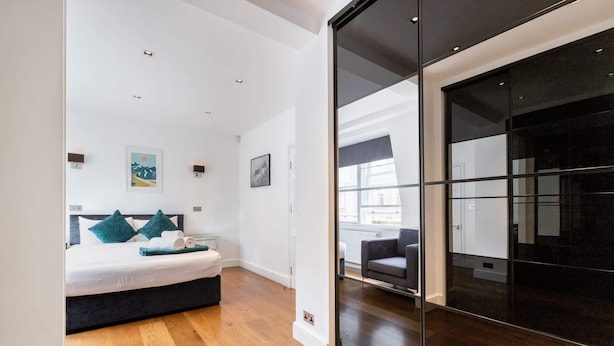 Ett modernt hotellrum med en stor säng, en mörk skjutdörr och utsikt över staden genom stora fönster.