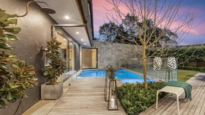A modern outdoor pool area with a wooden deck, a glass-enclosed hot tub, and a stone wall. - HUNTER VILLA - THE VINTAGE (POKOLBIN)