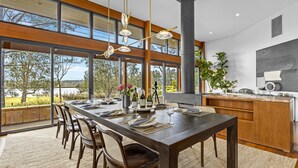 A modern dining area with a long table, chairs, and a view of the outdoors. - HUNTER VILLA - THE VINTAGE (POKOLBIN)