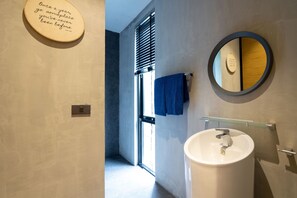 Un baño moderno con un espejo redondo, un lavabo blanco y una toalla colgada en la pared.