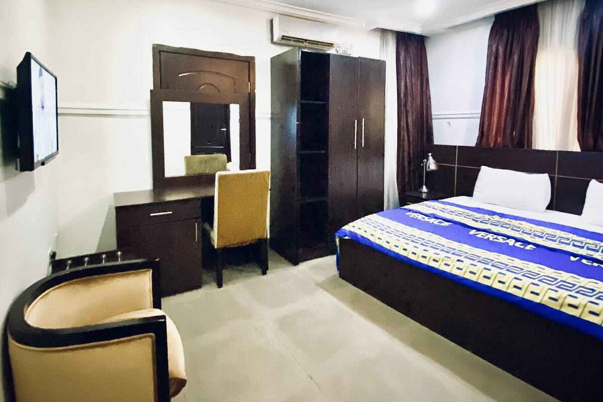 Una habitación de hotel con cama, escritorio, silla, armario y televisor.
