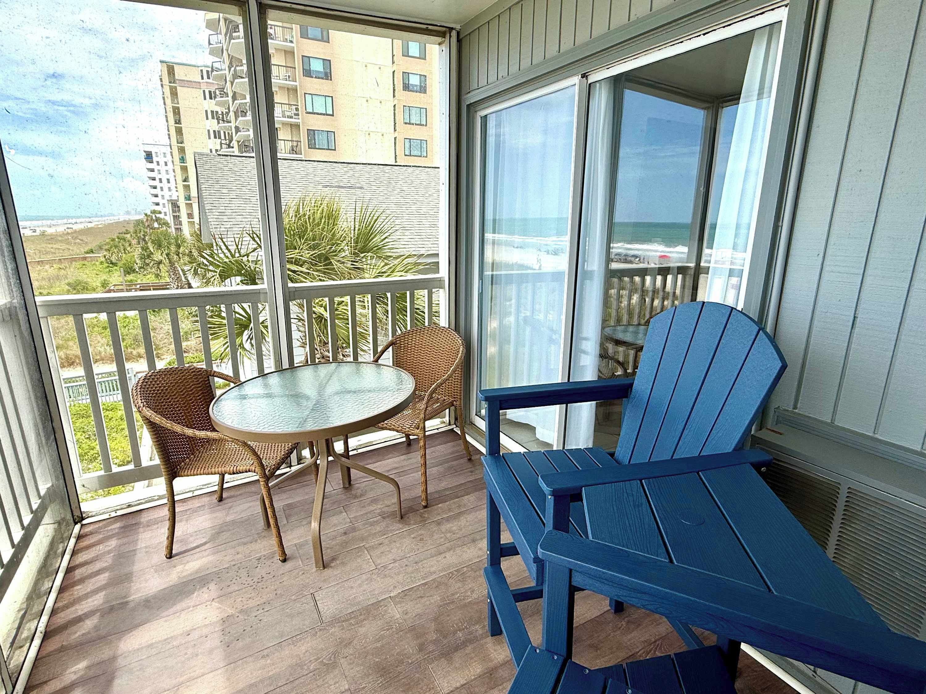 Ein Balkon mit einem runden Glastisch, zwei Korbstühlen und einem blauen Adirondack-Sessel.