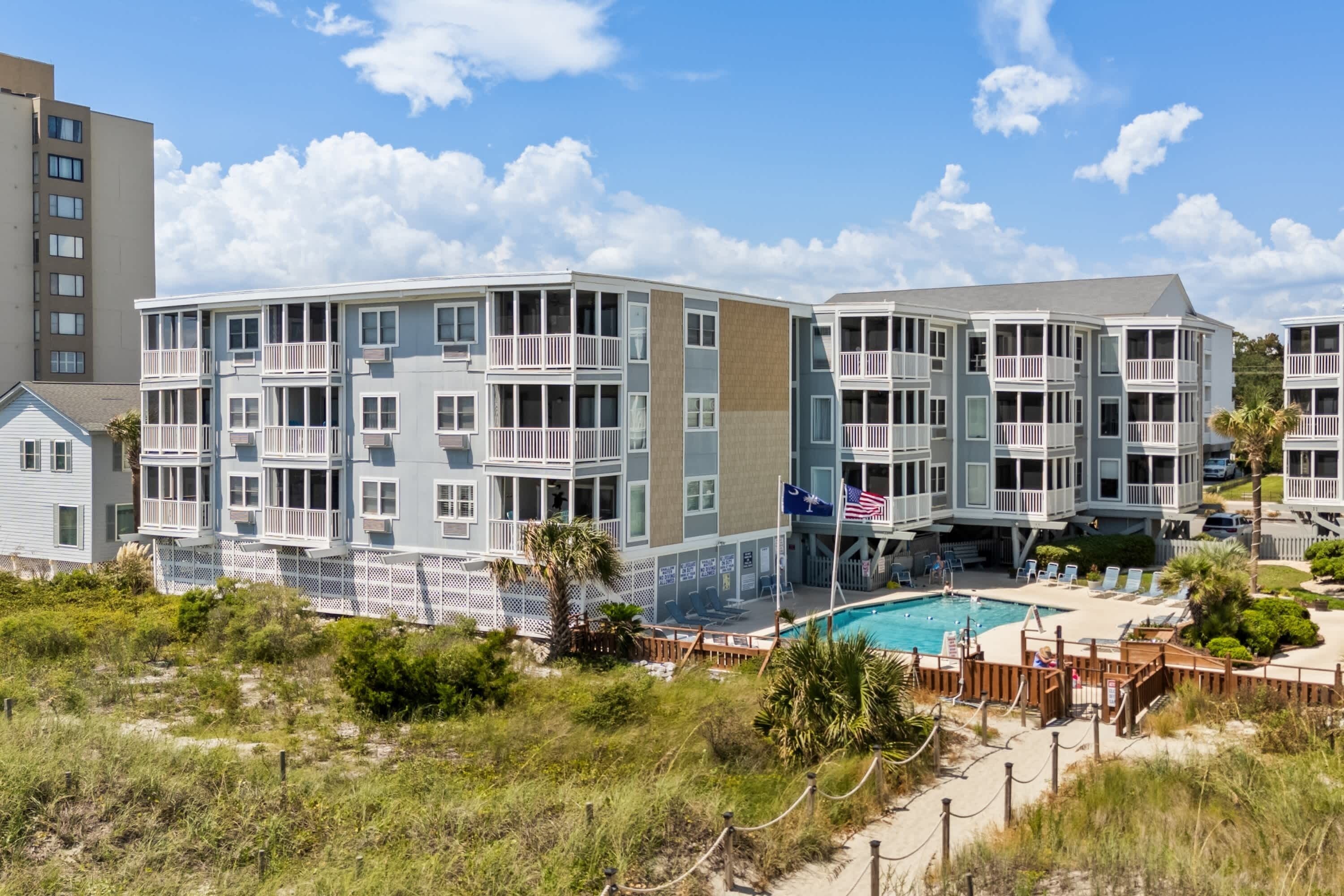 Ein Strandhotel mit mehreren Balkonen, einem Schwimmbad und einer Sandstrandanlage.