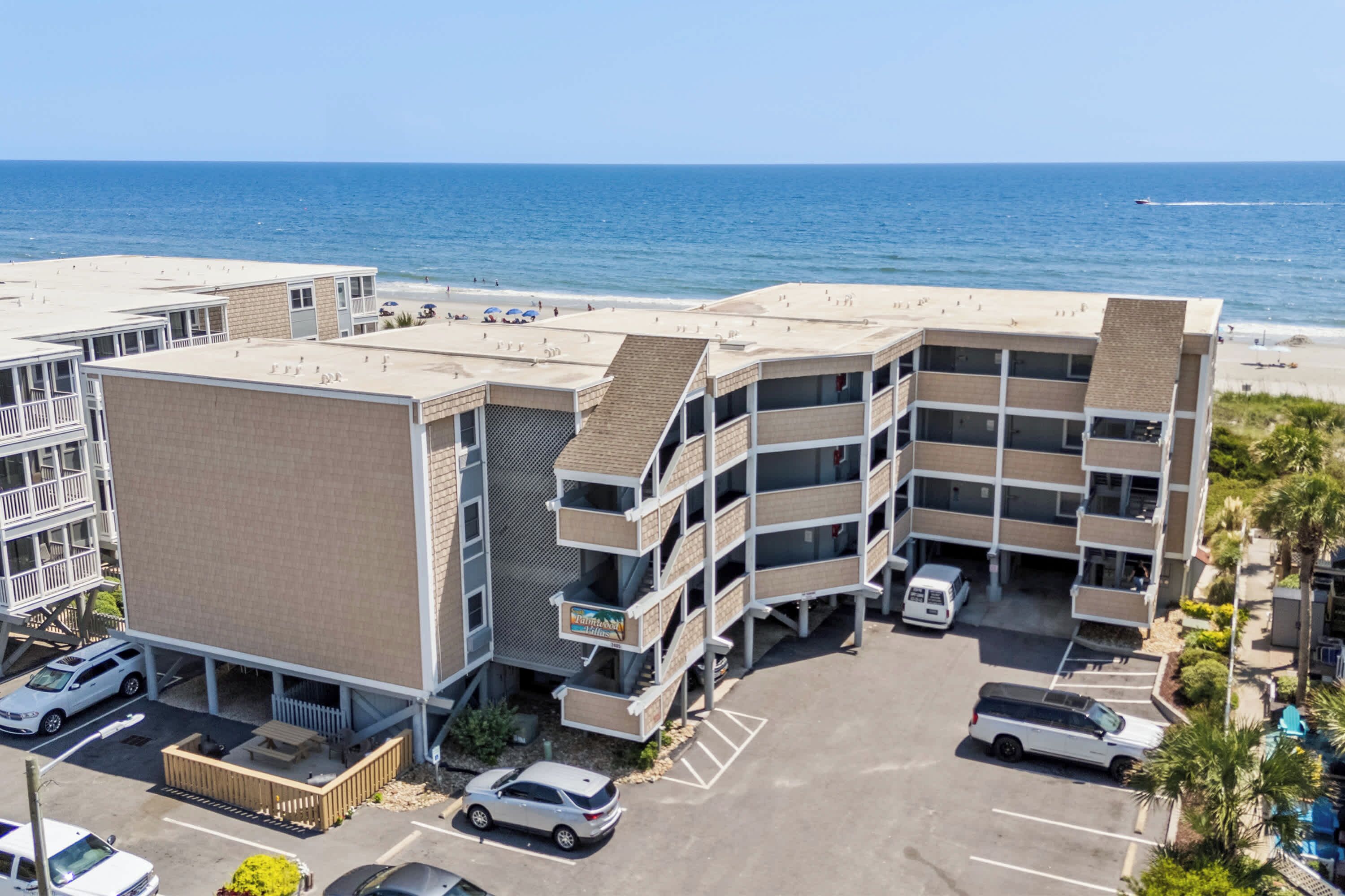 A multi-story hotel with a parking lot and a view of the beach.