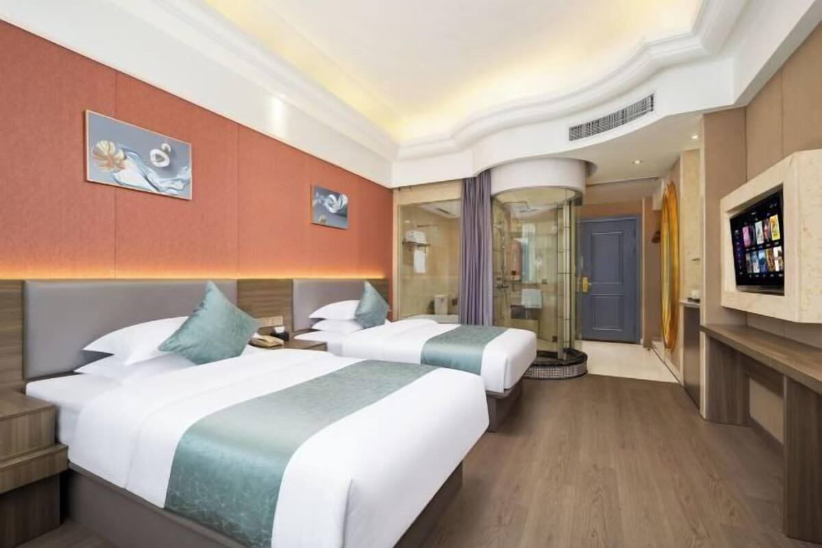 A hotel room with two beds, a TV, and a bathroom with a glass shower.