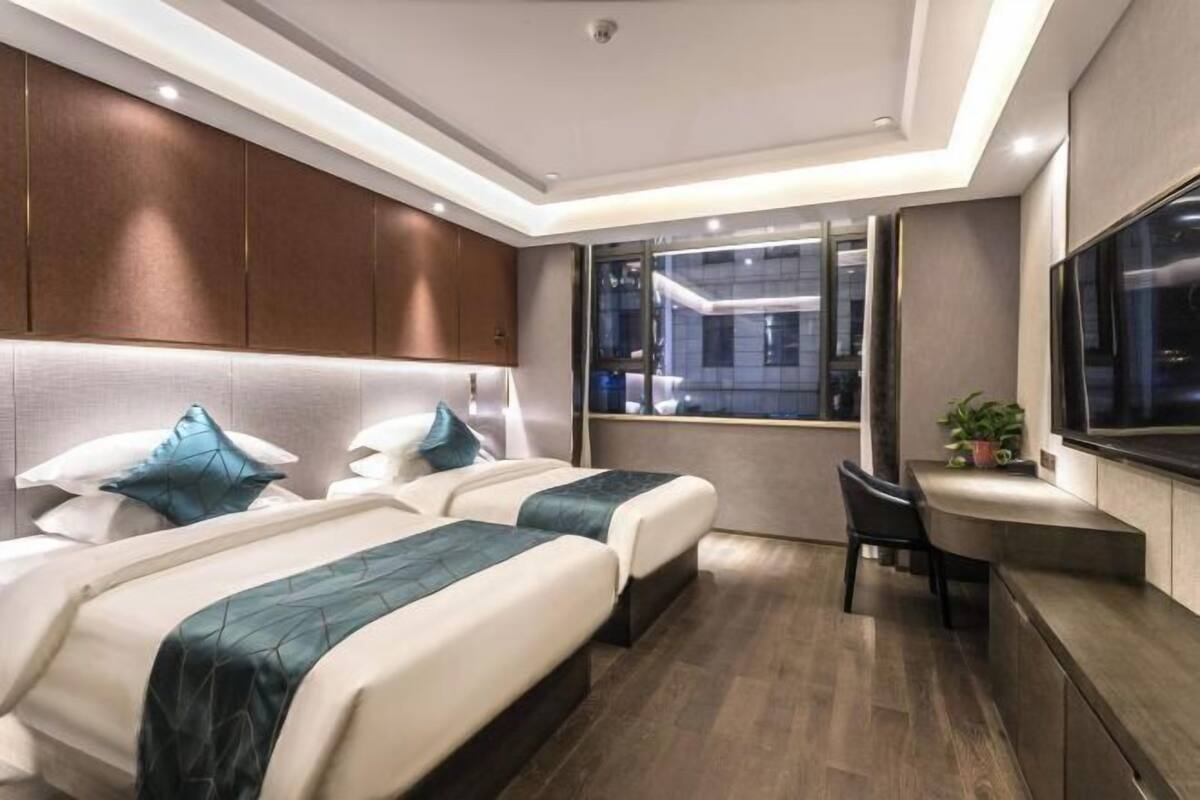 A modern hotel room with two beds, a desk, and a large window.