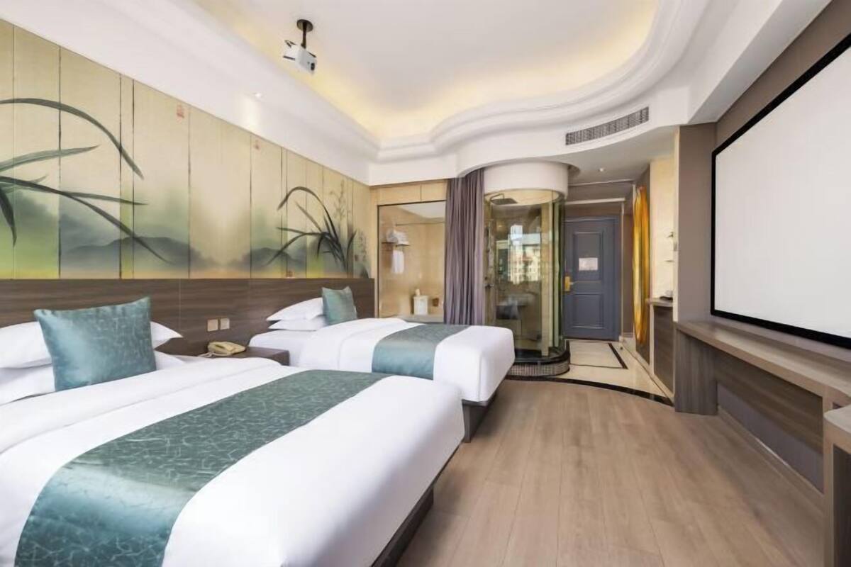 A hotel room with two beds, a large screen, and a glass elevator.