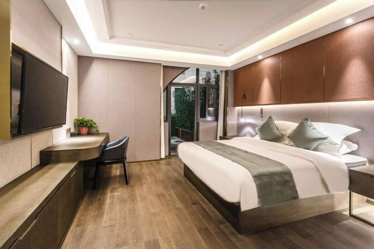 A modern bedroom with a large bed, a desk, and a TV.