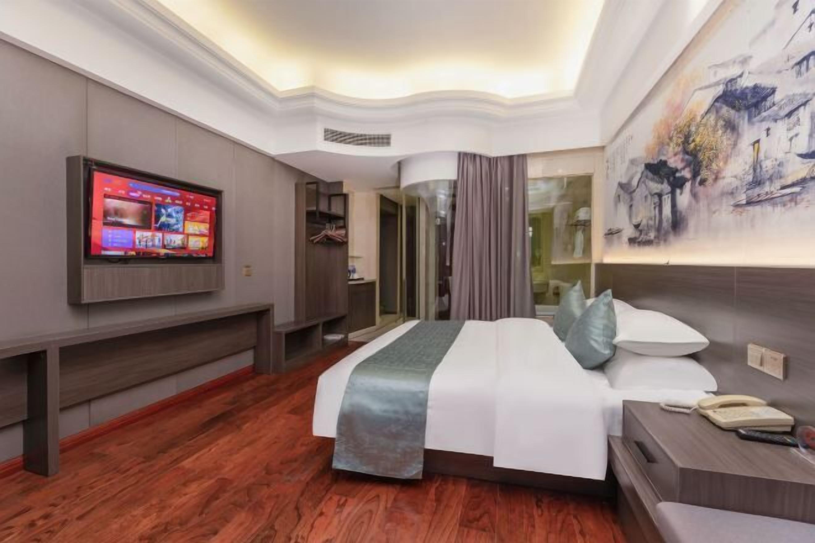 Une chambre d’hôtel moderne dotée d’un grand lit, d’un téléviseur à écran plat fixé au mur, d’une table de chevet avec un téléphone et d’un tableau accroché au mur.