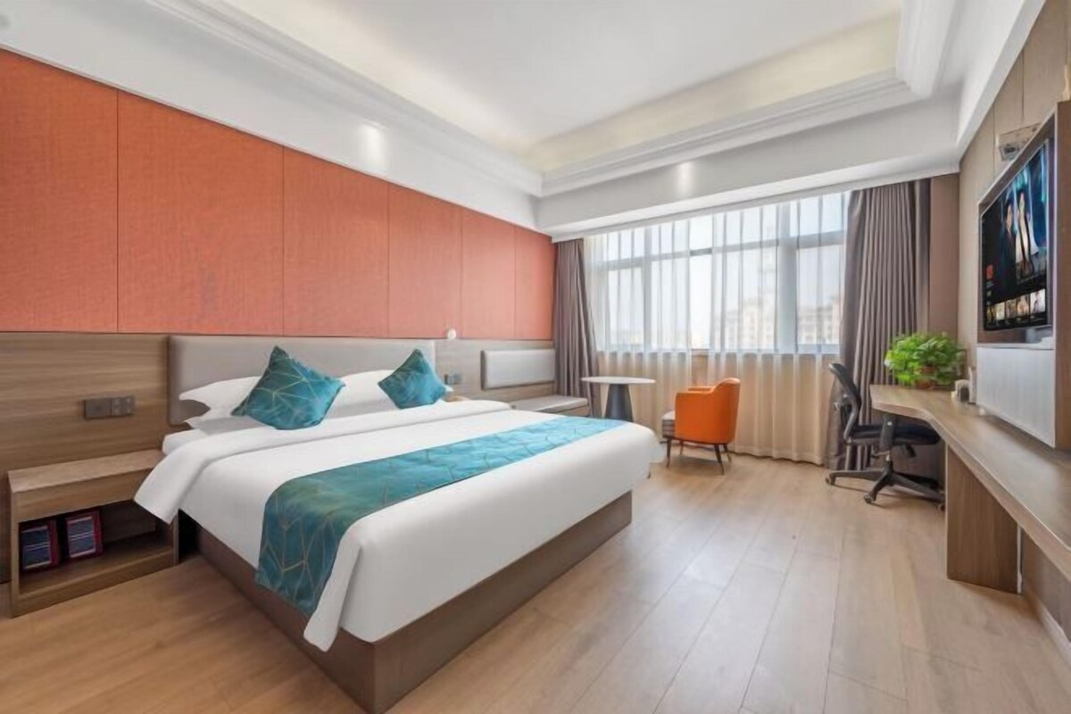 A hotel room with a large bed, a desk, a chair, and a TV.