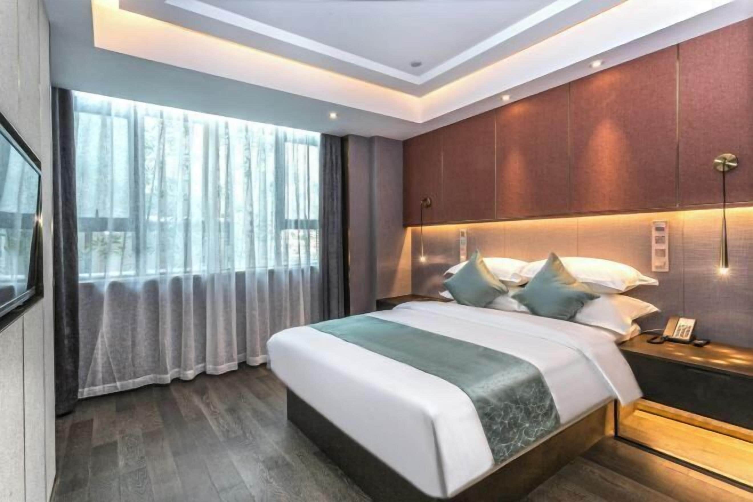 Una habitación de hotel moderna con una cama grande, una mesita de noche, un teléfono en la pared y una ventana con cortinas.