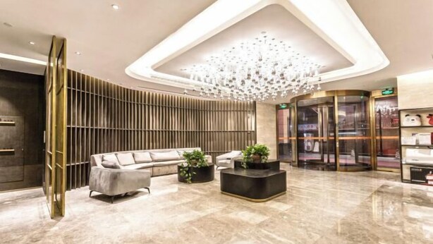 A modern lobby with a central seating area, a chandelier, and a glass elevator. - Fujun Meicheng Hotel (Suzhou)