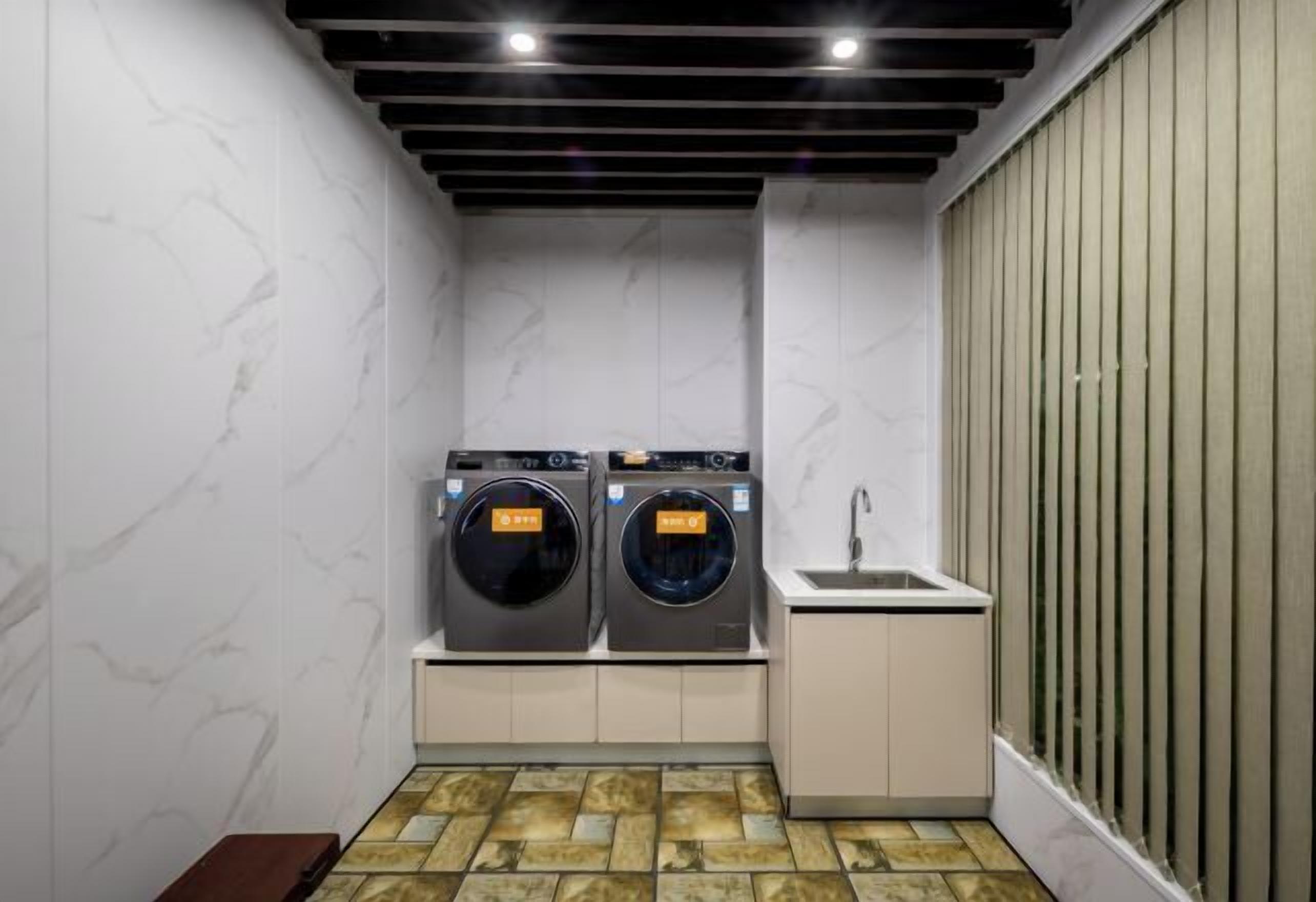 A compact laundry area with two front-loading washing machines, a sink, and a bench.