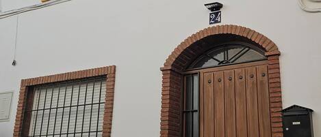 Ein zweistöckiges Gebäude mit weißer Fassade, gelben Fensterrahmen und einer braunen Tür.