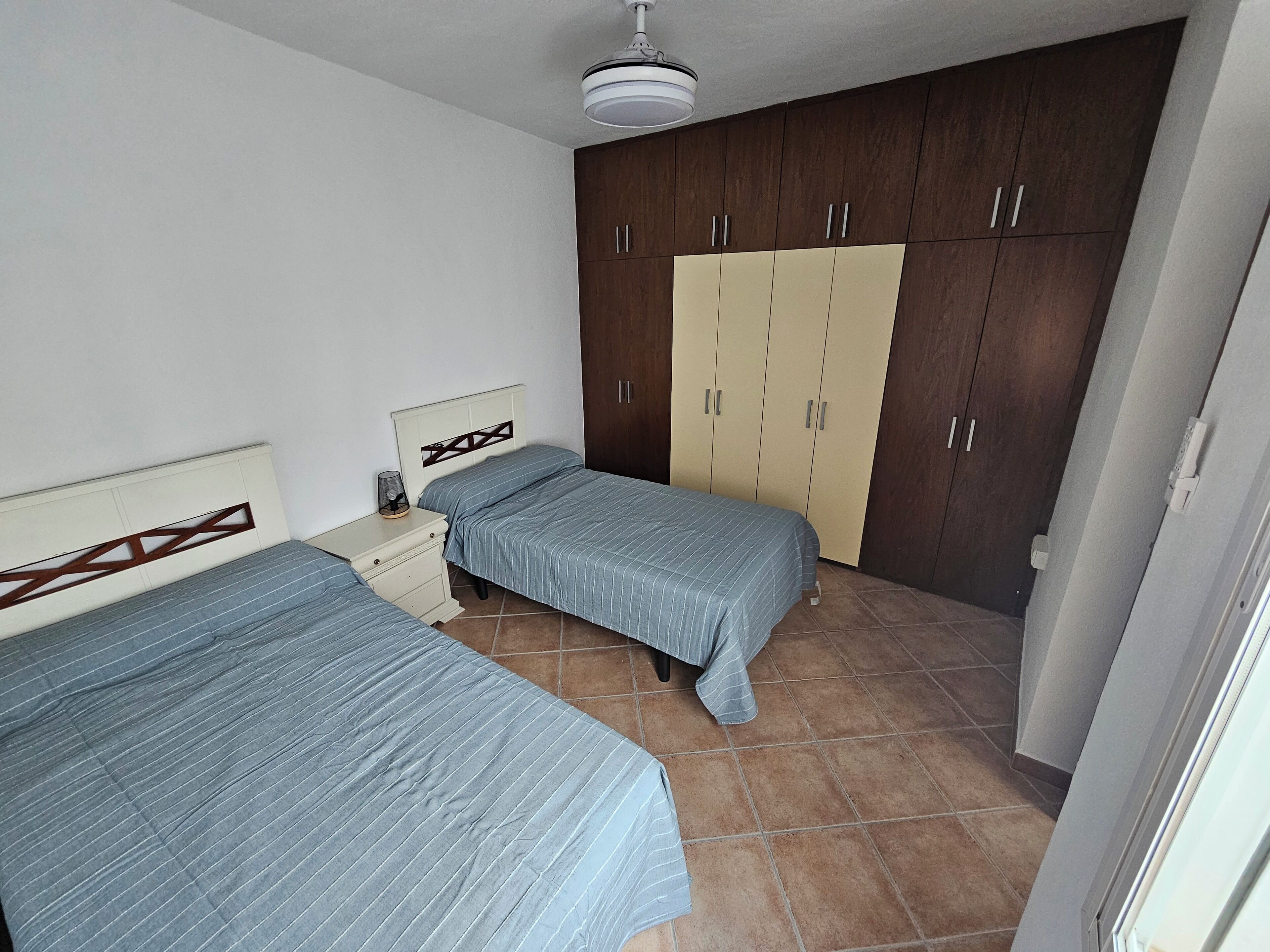 Een slaapkamer met twee eenpersoonsbedden, een kledingkast, een nachtkastje en een plafondventilator.