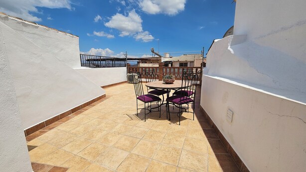 Una terraza en la azotea con una mesa redonda y sillas, rodeada de paredes blancas y suelo de baldosas.